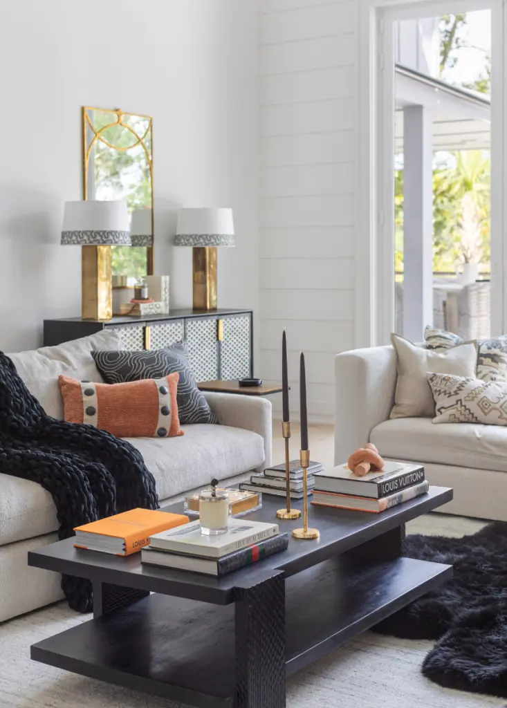 This contemporary coastal living room, styled by CHD interior designers, features a sleek, modern coffee table paired with cozy coastal couches, throws, and accent pillows.