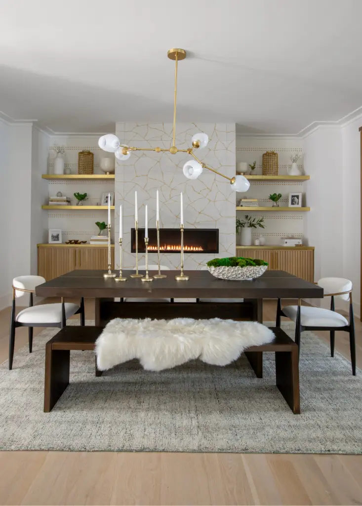 This dining room includes a polished dark wood table, styled with a plush, furry throw blanket over the bench seat. Our interior designers added chairs with a modern profile to each end, upholstered in a soft beige fabric for a touch of coastal interior design.