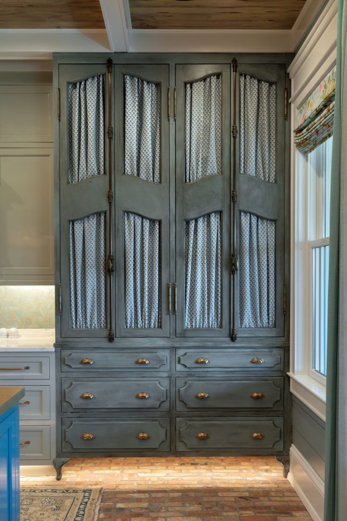 Palm Beach interiors kitchen featuring a tall gray cabinet with fabric-paneled doors, brass hardware, and built-in drawers in Georgetown, SC